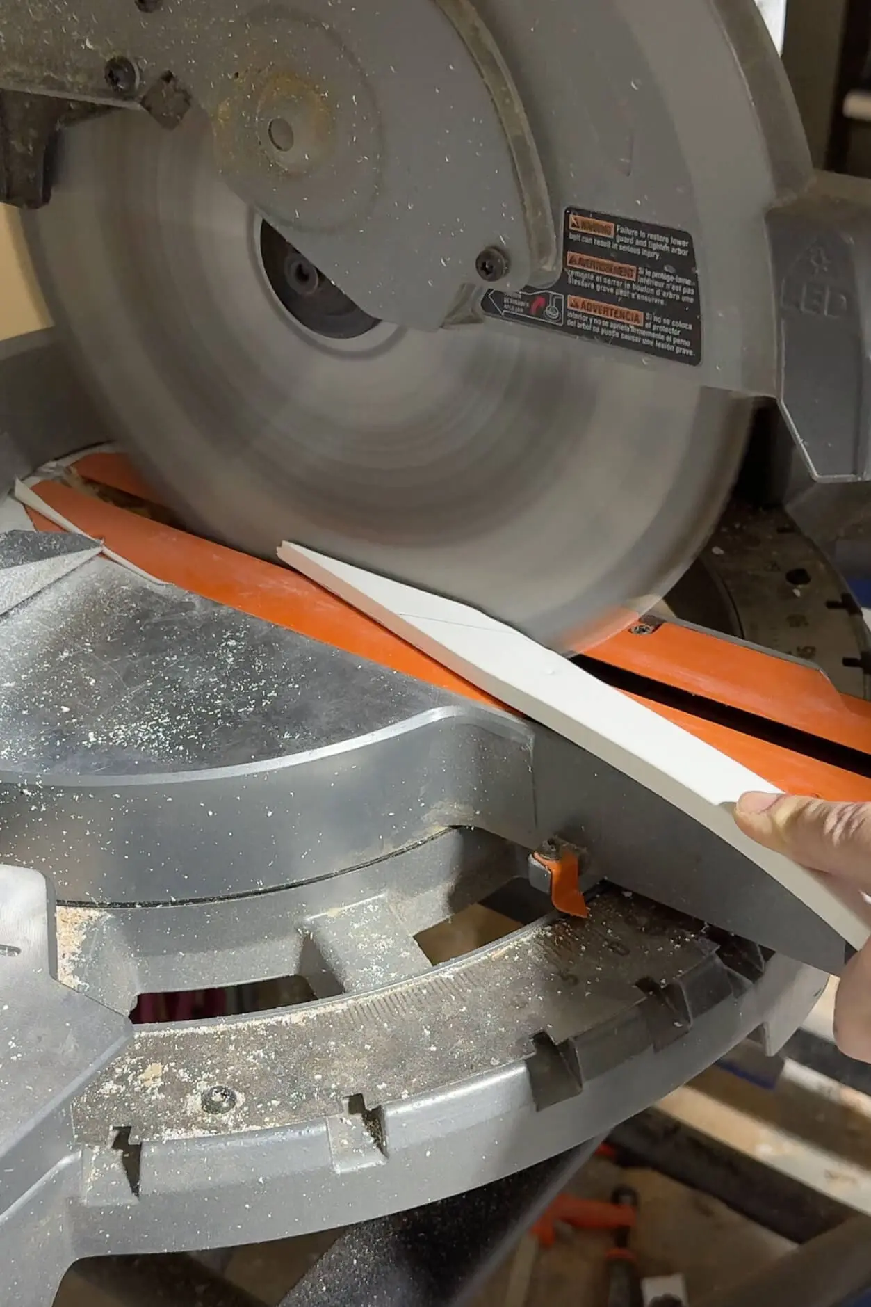 Action shot of a miter saw cutting through a white trim piece with precision. The orange safety features and visible sawdust highlight the tools and craftsmanship involved in this home project.